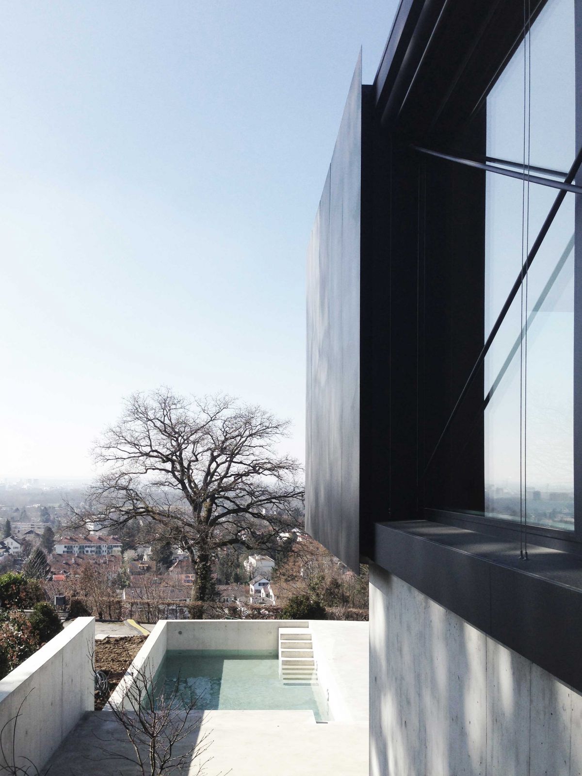 Die abgetreppten Aussenflächen aus Beton folgen dem gewachsenen Terrain und umfassen den Pool raeber_pool_sicht_von_eingang_aus