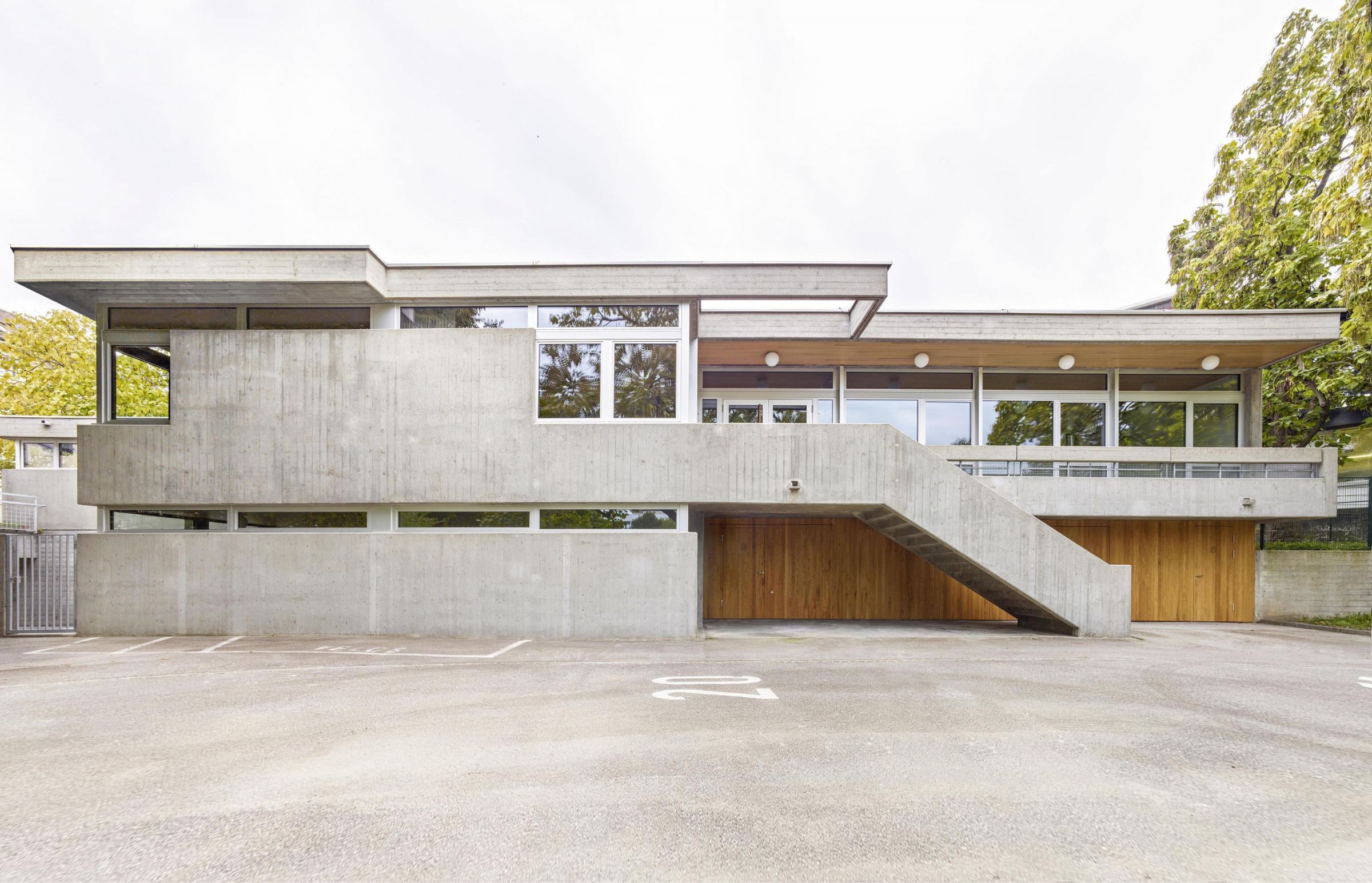 Die Betonfassade erscheint nach einer umfangreichen Sanierung wieder in ihrem ursprünglichen, rohen Sicht-Charakter und bildet zusammen mit den Holz-Metall-Fenstern in Aluminium das robuste Kleid des Hauses. 1_Verkehrsgarten_Nordfassade_Lukas_Raeber_Architekten_%C2%A9Weisswert_ms_1